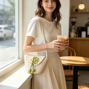 Peut inclure: Un sac bandoulière tissé de couleur crème doté d'un rabat orné de deux fleurs en tissu vert clair avec des centres jaunes et deux breloques pendantes en forme de feuille verte attachées par de fines cordes vertes, avec une bandoulière assortie.