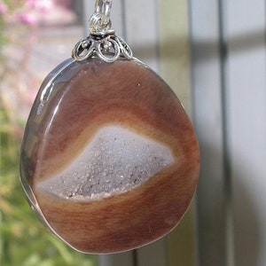 May include: A brown agate pendant with a white crystal center, set in a silver filigree bail.