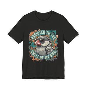 May include: A black short-sleeved t-shirt featuring a graphic of a bird wearing sunglasses. The bird is surrounded by colourful graffiti-style paint splatters and the text ADDICTED TO THE SMELL OF MY BIRD in a circular teal font around the illustration.