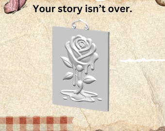 May include: A rectangular light gray plaque featuring a raised relief of a melting rose with a small hanging loop at the top. The text Your story isn't over. is printed in black above the plaque, with a pink butterfly and clock.
