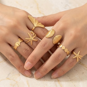 Puede incluir: Un conjunto de seis anillos en tono dorado con varios diseños inspirados en el océano, que incluyen dos formas de estrella de mar, dos motivos de concha de vieira, una pieza en forma de abanico y una banda compuesta por pequeños discos.