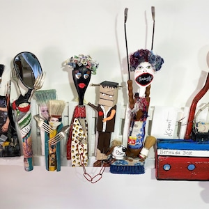 May include: A collection of mixed-media sculptures crafted from household items including spoons, forks, paintbrushes, and a small wooden boat labeled Bermuda Belle. The figures feature painted faces, fabric clothing, and various found objects as accessories.