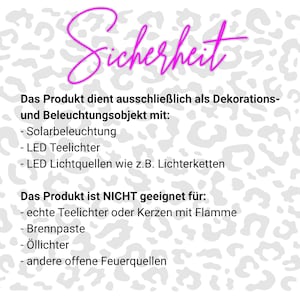 May include: A white sign with a gray leopard print pattern featuring the magenta text "Sicherheit" at the top. The text lists decorative and lighting uses including solar, LED tea lights, and string lights, while prohibiting open flames and oil.