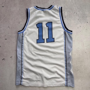 Op de afbeelding: Een wit mouwloos basketbalshirt met het nummer 11 in lichtblauw met een donkerblauwe omlijning. Het kledingstuk heeft donkerblauwe en lichtblauwe biezen bij de hals en armsgaten, met lichtgrijze zijpanelen voorzien van een wit ruitpatroon.
