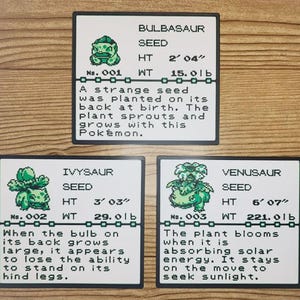 May include: Three rectangular white cards featuring pixelated green illustrations of Bulbasaur, Ivysaur, and Venusaur. Each card displays the Pokémon name, number, height in feet and inches, weight in pounds, and a descriptive text block.
