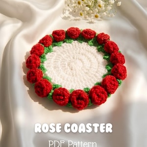 May include: A round white crocheted coaster featuring a border of small red roses with green leaves. The text ROSE COASTER PDF Pattern By MiMi Crochet is printed below the coaster. The design is circular with a textured yarn finish.