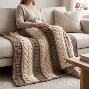 May include: A knitted throw blanket featuring alternating vertical stripes of cream-colored cable knit patterns and textured dark brown panels. The blanket is draped over a lap, showcasing a thick, chunky yarn construction with a repeating braided design.