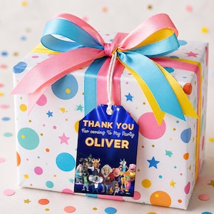 May include: A square gift box wrapped in white paper with colorful polka dots and stars, topped with a large pink, blue, and yellow ribbon. A blue rectangular tag hangs from the ribbon, featuring the text THANK YOU For coming To My Party OLIVER.