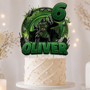 Peut inclure: Une décoration de gâteau circulaire verte illustrant le personnage Docteur Doom, le chiffre 6 et le nom OLIVER en lettres vertes épaisses. La décoration est placée sur un gâteau au glaçage blanc orné de petites perles blanches.