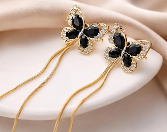 Pendientes de cadena con mariposa negra y borla de diamantes de imitación dorados.