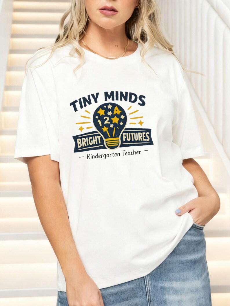 May include: A white short-sleeve t-shirt featuring a graphic of a lightbulb filled with stars and the number 12. The text reads "TINY MINDS BRIGHT FUTURES" and "Kindergarten Teacher" in dark blue and yellow ink on the front of the garment.