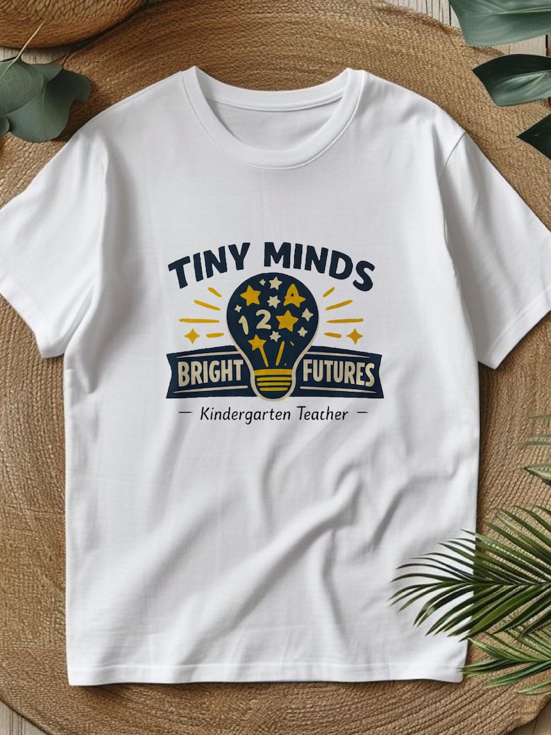 May include: A white short-sleeved t-shirt featuring a graphic of a dark blue lightbulb filled with yellow stars and the number 12. The text reads "TINY MINDS BRIGHT FUTURES" and "Kindergarten Teacher" in dark blue and yellow lettering.