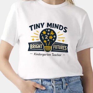 May include: A white short-sleeved t-shirt featuring a graphic of a dark blue lightbulb filled with yellow stars and the number 12. The text reads TINY MINDS BRIGHT FUTURES and Kindergarten Teacher in dark blue and yellow lettering.