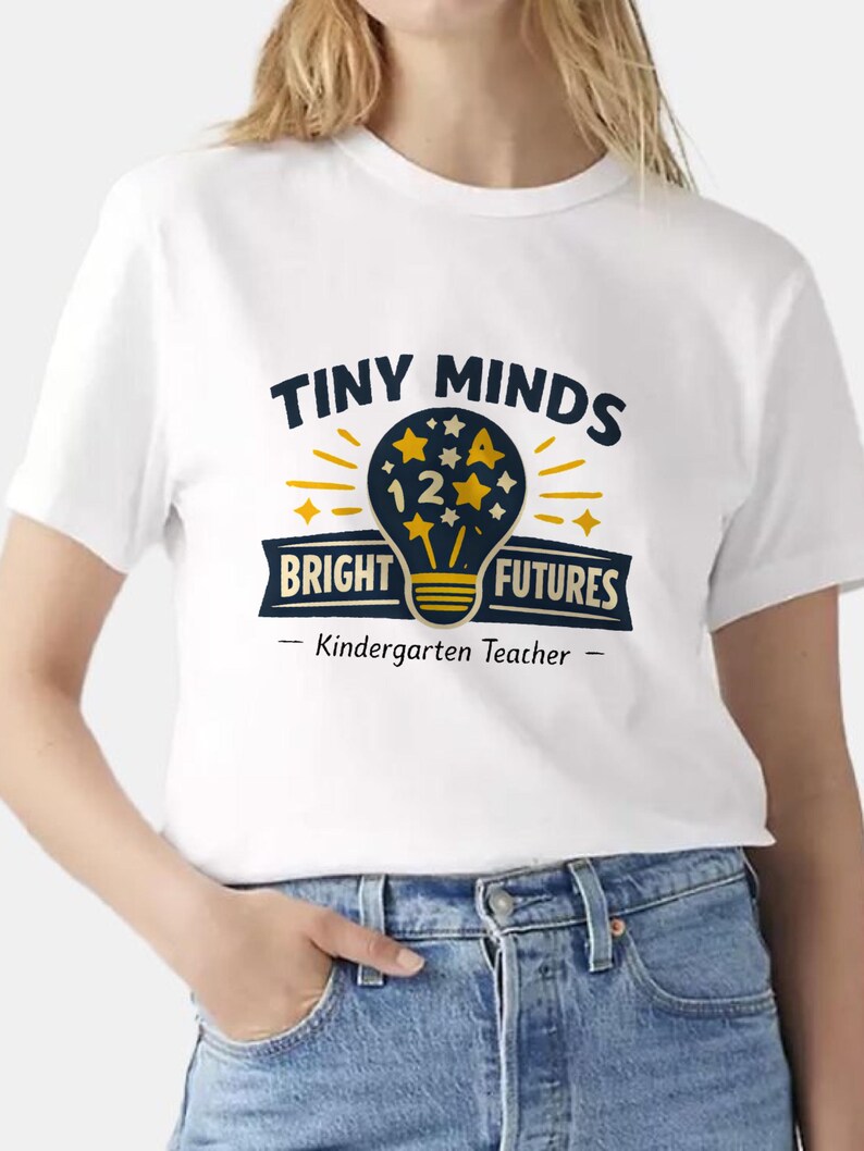 May include: A white short-sleeved t-shirt featuring a graphic of a dark blue lightbulb filled with yellow stars and the number 12. The text reads TINY MINDS BRIGHT FUTURES and Kindergarten Teacher in dark blue and yellow lettering.