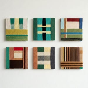 Op de afbeelding: Een set van zes vierkante wandkunstwerken met ingewikkelde garenwikkelingen in diverse geometrische patronen. De collectie toont een gevarieerd kleurenpalet met tinten groen, bruin, crème, zwart, rood en blauw met textuurrijke vezels.