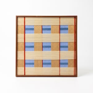 May include: A square wall art piece featuring a grid of woven light tan and blue threads encased in a thin brown wooden frame. Two vertical red threads run across the surface, intersecting with horizontal bands of tan and blue woven textures.