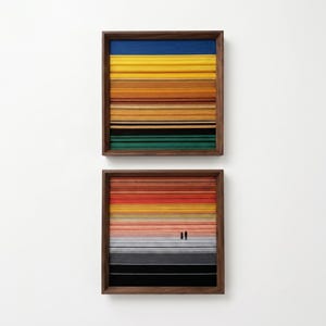 Könnte beinhalten: Zwei quadratische Wandbilder in dunklen Holzrahmen mit horizontal geschichteten Streifen aus farbigem Material. Das obere Bild zeigt blaue, gelbe, orange, braune und grüne Bänder. Das untere Bild zeigt rote, orange, gelbe und graue Verläufe mit zwei kleinen schwarzen Silhouetten von Figuren, die in der Mitte stehen.
