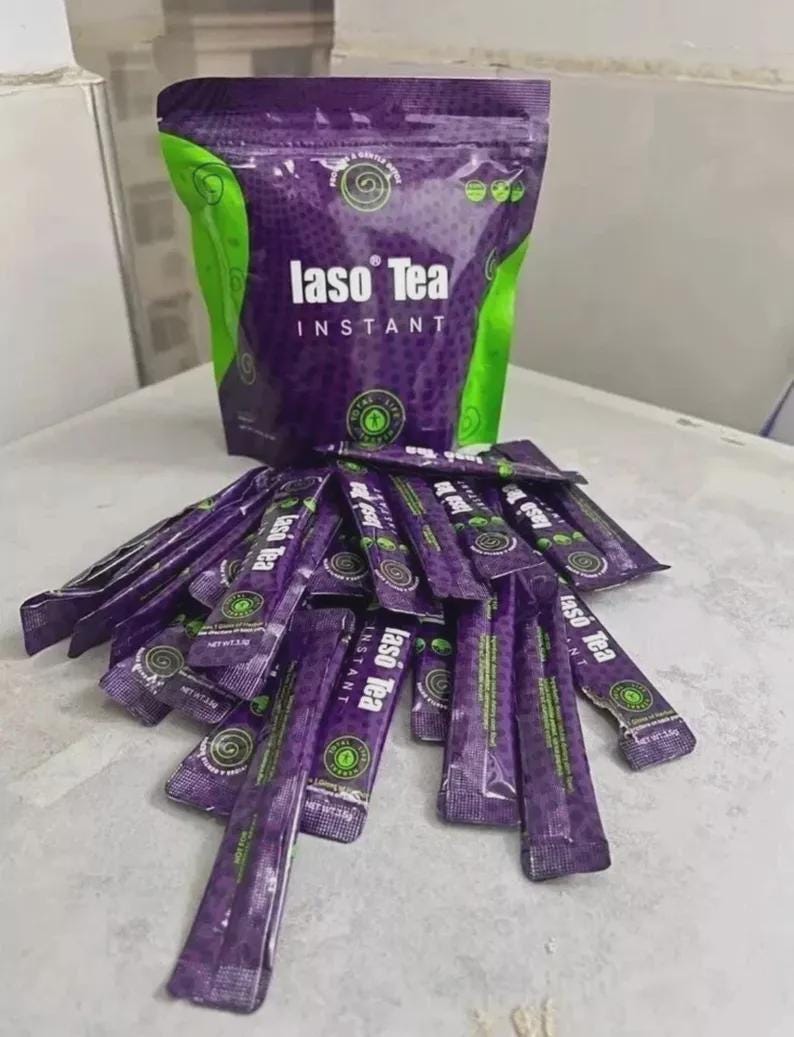 May include: A large purple and green pouch of Iaso Tea Instant with a pile of matching individual tea stick packets spread out in front. The packaging features the brand name Iaso Tea in white text, along with circular green logos and patterns.