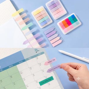 May include: A collection of translucent, arrow-shaped adhesive page markers in pastel and vibrant colors, organized in clear plastic dispensers. The markers are shown applied to a grid notebook and a monthly calendar with handwritten text.