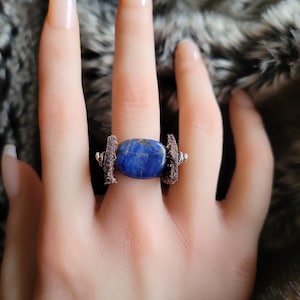 May include: A ring with a large, oval-shaped blue lapis lazuli stone set in a brown leather band with silver accents.