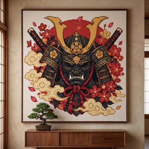 May include: A square cross-stitch pattern featuring a black samurai helmet with gold accents, two crossed katanas, and red cherry blossoms. The design is set against a large red circle with stylized beige clouds on a white fabric background.