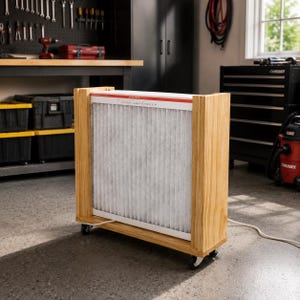 May include: A rectangular air purifier unit featuring a pleated white filter panel held within a light-toned wooden frame. The base is equipped with four small black caster wheels for mobility, and a white power cord extends from the bottom side.