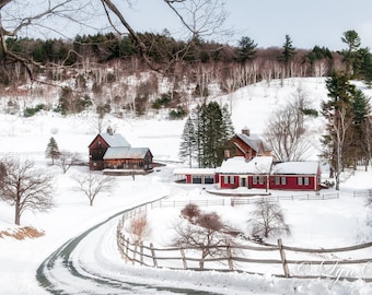May include: A snowy winter scene with a red farmhouse and a barn in the background. The farmhouse has a white roof and a porch. The barn is a darker red and has a wooden roof. There are trees in the foreground and background, and the ground is covered in snow.
