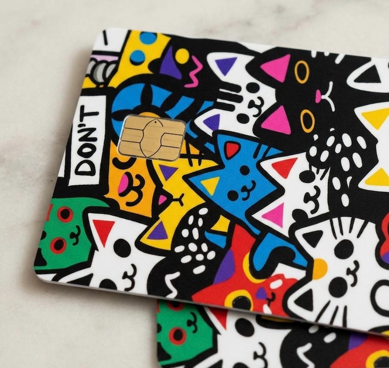 May include: A rectangular credit card skin featuring a vibrant, multi-colored cartoon pattern of various cats in black, white, yellow, blue, green, and red. The design includes the text DON'T printed in black on a white rectangular background.
