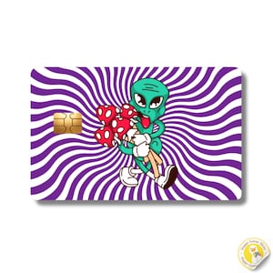 May include: A rectangular credit card skin featuring a purple and white radial swirl pattern. In the centre, a green cartoon alien with large eyes and a tongue sticking out holds a bouquet of red and white spotted mushrooms with white stems.