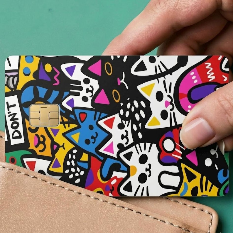 May include: A rectangular credit card featuring a vibrant, multi-colored doodle pattern of various cats in black, white, yellow, blue, red, and pink. The card includes a gold-colored EMV chip and the text DON'T printed vertically on the left side.