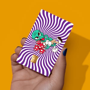 May include: A rectangular credit card skin featuring a vibrant purple and white wavy spiral pattern. In the centre, a green cartoon alien with large black eyes is depicted holding a cluster of red mushrooms with white spots, wearing white gloves.