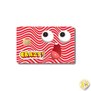 May include: A rectangular credit card skin featuring a red and pink wavy line pattern. The design includes two large white cartoon eyes with black pupils, an open mouth with a pink tongue, and the yellow text CRAZY! with a white outline.