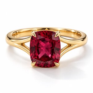 Può includere: Un anello in oro con una grande pietra preziosa rosso intenso a taglio cuscino, fissata da una montatura a quattro griffe. La fascia in oro giallo lucido si divide in due rami distinti verso la pietra centrale, creando un design aperto.