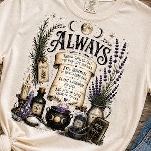 May include: A cream-colored t-shirt featuring a graphic print with the text ALWAYS and instructions for luck. The design includes illustrations of a rosemary sprig, a scroll, a candle, a salt bottle, a cauldron, lavender, and a book of spells.