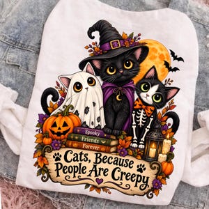 May include: A white t-shirt featuring a graphic of three cats: one dressed as a ghost, one as a witch, and one in a skeleton costume. They sit on books labelled Spooky, Friends, Forever, next to a pumpkin and lantern. Text reads: Cats, Because People Are Creepy.