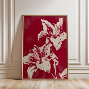 May include: A rectangular wall art print in a thin wooden frame featuring a deep red background with a textured finish. The artwork displays two large, off-white lily flowers rendered in a bold, painterly style with visible brushstrokes.