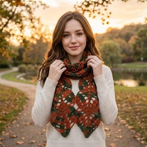 May include: A crochet scarf featuring a repeating leaf pattern in variegated shades of burnt orange and forest green. The scarf is worn wrapped around the neck, showcasing an intricate openwork design with pointed, leaf-shaped ends.
