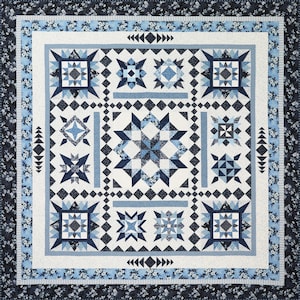 May include: A square quilt featuring a central large star block surrounded by smaller star and geometric blocks in shades of navy blue, light blue, and white. The quilt has a floral border and intricate pieced patterns throughout the design.