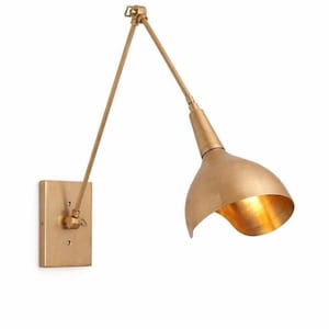 May include: A wall-mounted lamp with a brushed brass finish, featuring a rectangular backplate, a long adjustable swing arm with a central hinge, and a wide, bell-shaped shade that directs light downward from its metallic interior surface.