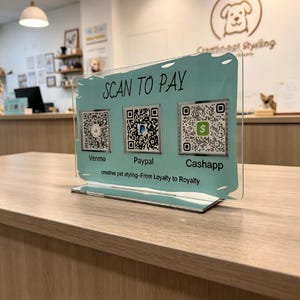 May include: A rectangular clear acrylic sign with a light blue background featuring the text SCAN TO PAY and three QR codes labeled Venmo, Paypal, and Cashapp. The bottom text reads creative pet styling-From Loyalty to Royalty.