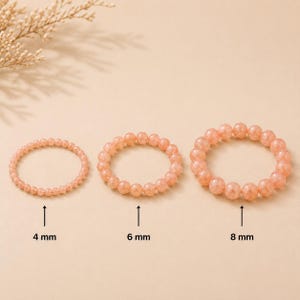 Può includere: Tre braccialetti circolari realizzati con perline traslucide e maculate color pesca. I braccialetti sono disposti per dimensione, con etichette che indicano diametri delle perline di 4 mm, 6 mm e 8 mm. Ogni braccialetto è composto da una fila.
