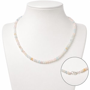 Op de afbeelding: Een kralenketting met kleine, gefacetteerde, doorschijnende stenen in zachte pasteltinten van lichtroze, lichtblauw en geel. De ketting is voorzien van een zilverkleurige metalen karabijnsluiting, getoond in een cirkelvormig detailvenster.