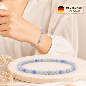 Könnte beinhalten: Ein Armband aus kleinen, facettierten hellblauen und mittelblauen Perlen in einem sich wiederholenden Muster. Das Armband ist sowohl am Handgelenk als auch kreisförmig auf einer strukturierten, runden steinartigen Oberfläche zu sehen.