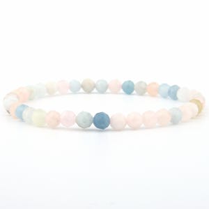 Könnte beinhalten: Ein elastisches Armband bestehend aus kleinen, runden, facettierten Perlen in verschiedenen sanften Pastellfarben wie Hellrosa, Hellblau, Creme und Weiß. Die Perlen sind in einem sich wiederholenden Muster angeordnet und bilden ein gleichmäßiges Band.