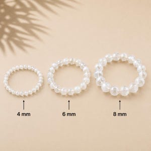 Könnte beinhalten: Drei kreisförmige Perlenarmbänder aus klaren, durchscheinenden Steinen. Die Armbänder sind nach Größe angeordnet, mit Beschriftungen, die Perlendurchmesser von 4 mm, 6 mm und 8 mm angeben. Jedes Armband besteht aus einer einzelnen Reihe runder Perlen.