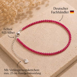 May include: A bracelet featuring small, faceted magenta beads and a silver-colored clasp. It includes a silver-colored extension chain with a small heart-shaped charm at the end. Text on the image includes "Echtes 925 Silber", "Deutscher Fachhändler", and "Mit Verlängerungskettchen: max. 23 cm Handgelenkumfang".