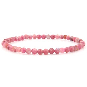 Könnte beinhalten: Ein kreisförmiges Armband aus kleinen, facettierten, runden rosa Perlen. Die Perlen weisen verschiedene Rosatöne auf, von hell bis kräftig, mit einer reflektierenden, facettierten Oberflächenstruktur, die dem gesamten Schmuckstück ein subtiles Funkeln verleiht.
