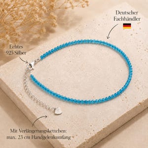 Könnte beinhalten: Ein hellblaues Perlenarmband mit einem Silberverschluss und einer verstellbaren Verlängerungskette. Das Schmuckstück hat einen kleinen herzförmigen Anhänger am Kettenende. Der Text gibt 925er Silber und 23 cm maximale Länge an.