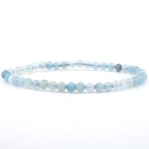 Könnte beinhalten: Ein zartes Perlenarmband aus kleinen, facettierten, runden hellblauen und durchscheinenden weißen Steinen. Die Perlen sind in einem durchgehenden kreisförmigen Muster aufgereiht und zeigen eine subtile Variation in Farbe und Textur bei jedem einzelnen Stein.