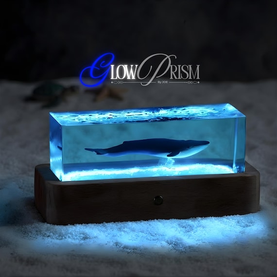 A whale silhouette cast in glowing epoxy resin and real wood — it's a night light, a sculpture, and a mood piece all in one desk object.